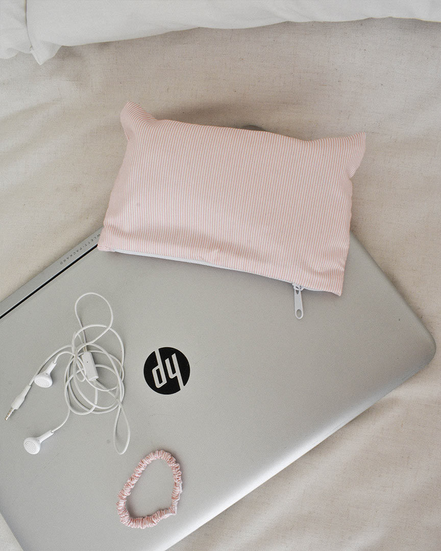 Pouch rosa Stripe fotografiado en ambiente sobre laptop HP con auriculaes blancos.